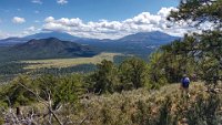 SuzannesPics-20190917 130314-HDR  Time to head down.  Bob takes the lead. What a view: That's Humphreys Peak (el. 12,633 ft) on the left horizon with its top in the clouds.  The mountain on the right is Kendrick (el. 10,425 ft) - it looks taller than Humphreys, but that is because it is closer.  That small mountain this side of Humphreys is Slate Mountain.  These are all part of the San Francisco Peaks and were once part of the same stratovolcano San Francisco Peak that exploded a couple of million years ago (let's just say before this day's hikers moved to AZ).